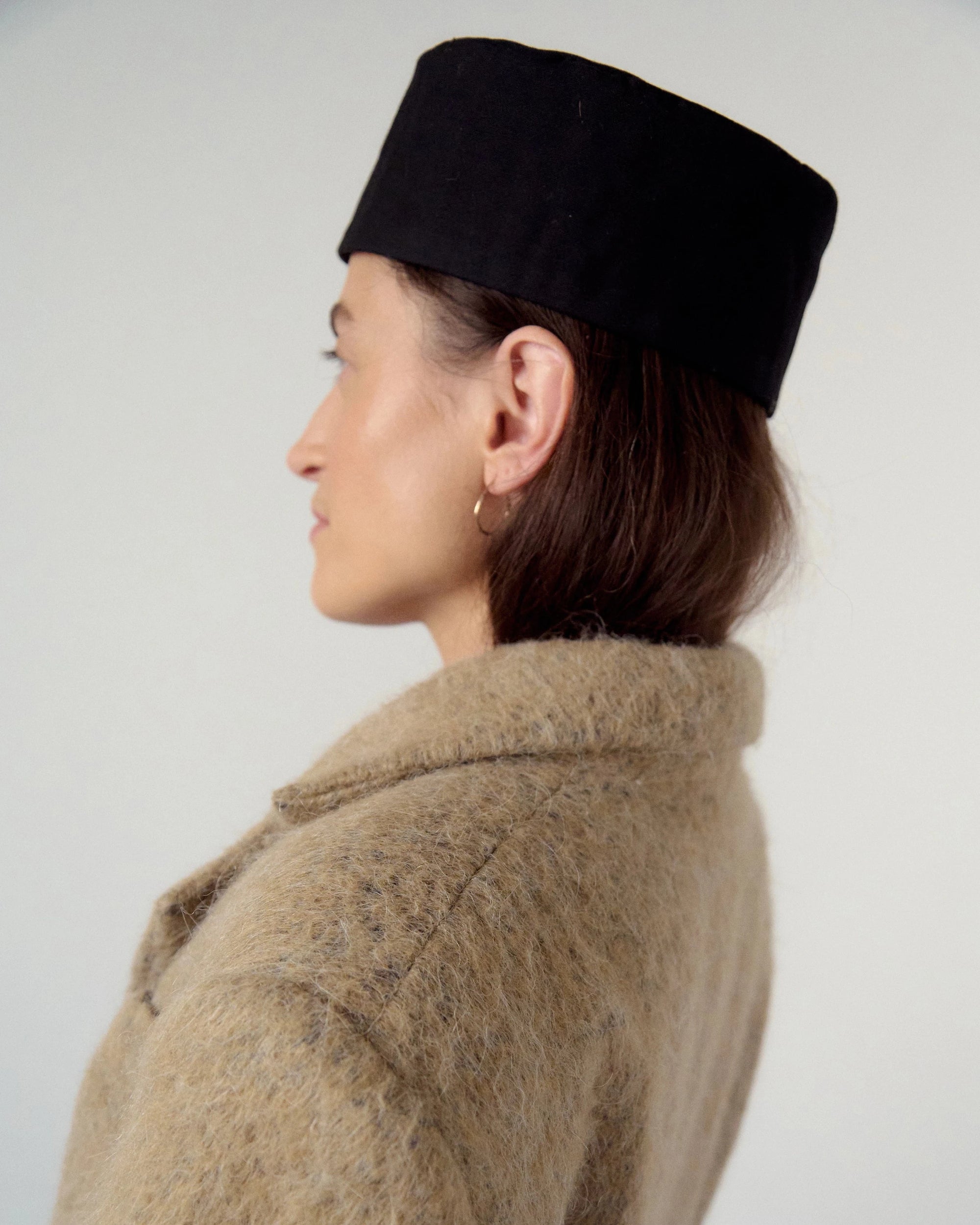 Woman wearing a beige, sand coat and black hat against a white background