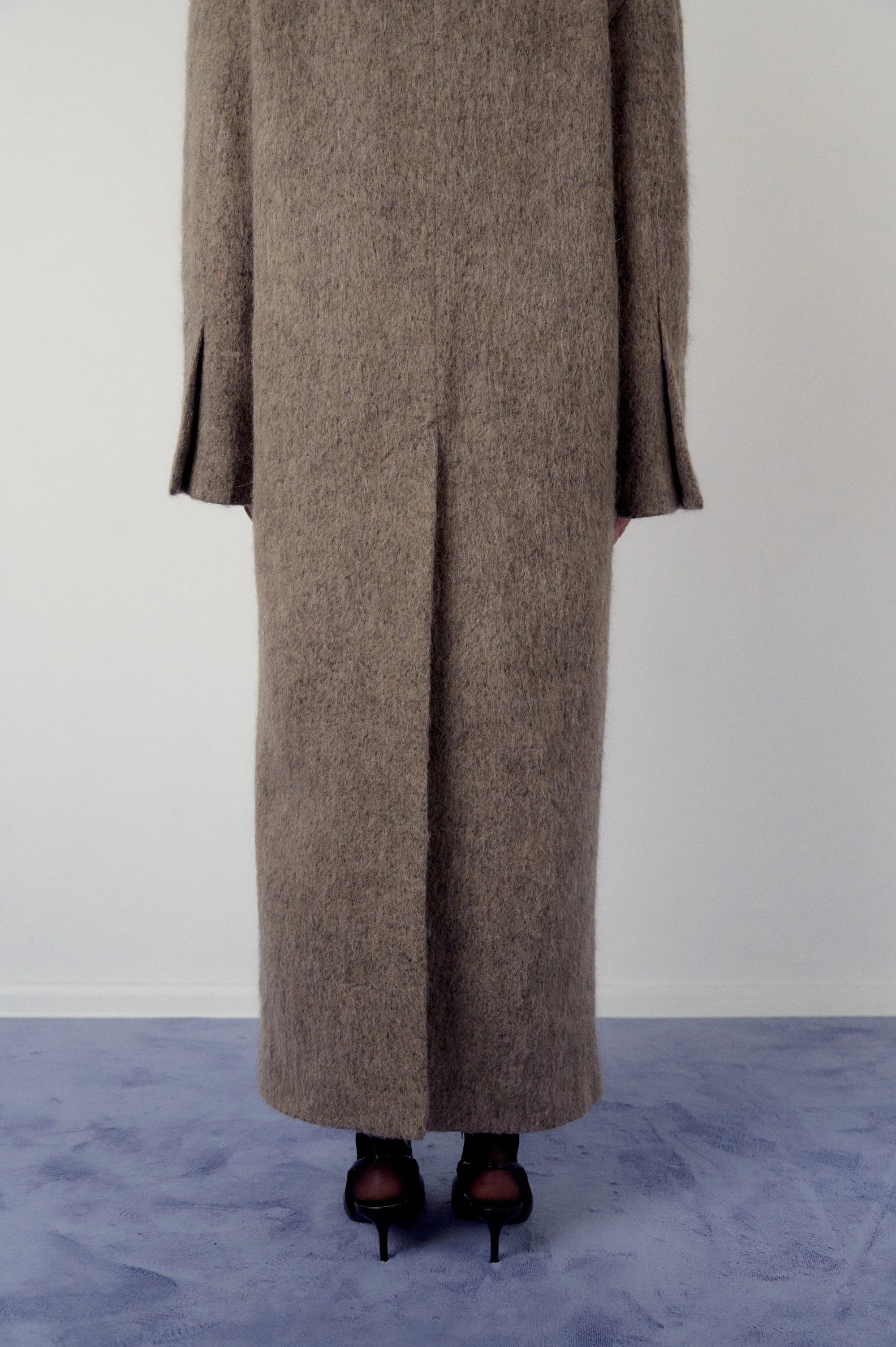 Woman wearing a long brown, warm grey coat on a plain background