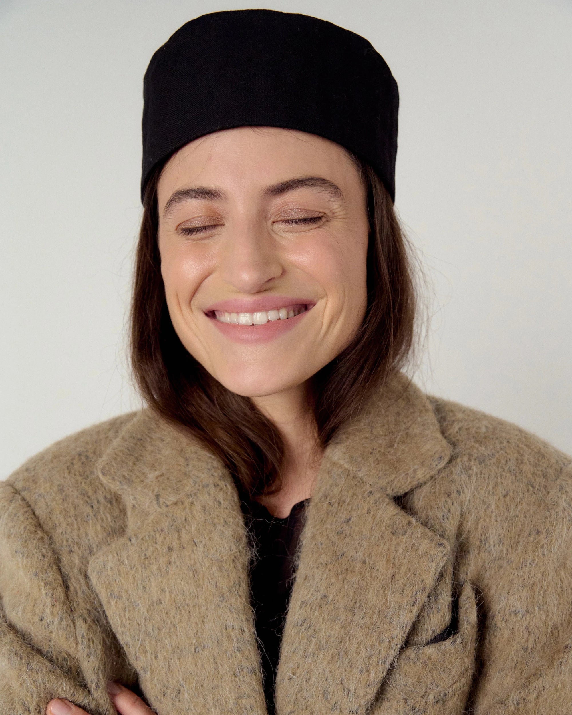 Woman wearing a black hat and beige, sand coat against a white background